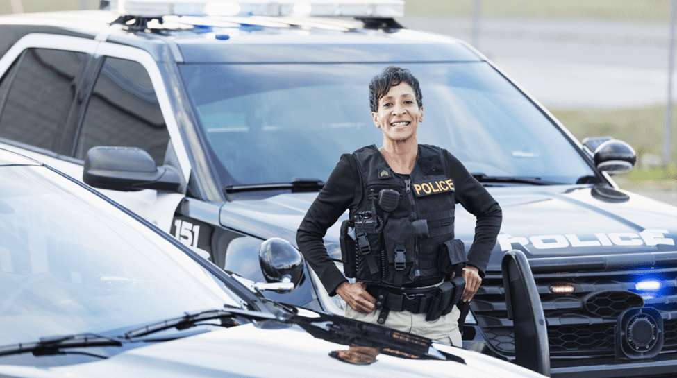 A woman in police uniform standing next to two cars.